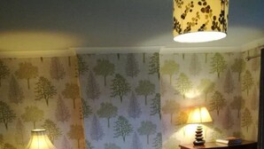Ett sovrum med en säng, två sängbord med lampor och en vägg med ett trädmönster.