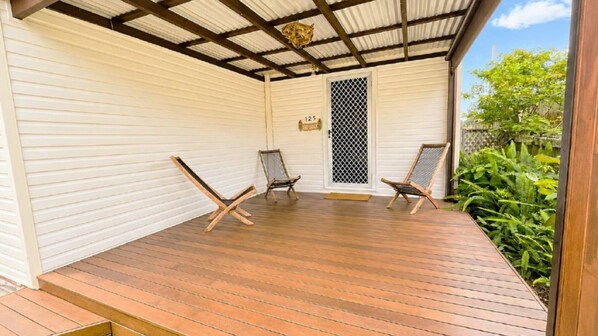 A covered porch with wooden flooring, two folding chairs, and a door with a mesh screen.