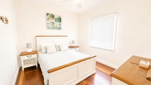 A bedroom with a bed, bedside tables, a nightstand, a window with blinds, and a ceiling fan.