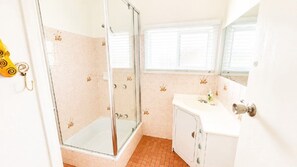 A bathroom with a glass shower enclosure, a sink with a mirror, and a door with a keyhole.