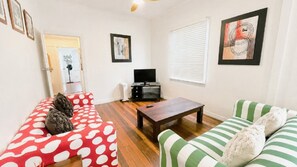 A living room with a sofa, a coffee table, and a TV stand. - Teke Cottage - traditional fishermans cottage (Wooli)