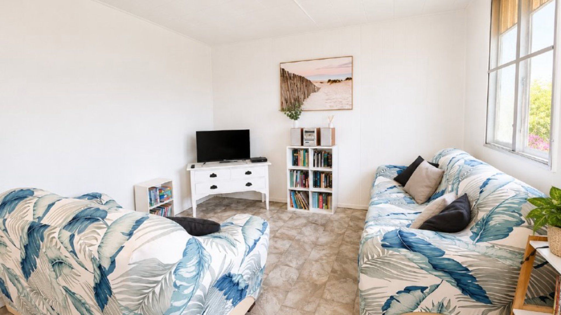 Una sala de estar con dos sofás, un televisor, una estantería y un cuadro en la pared.