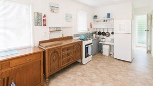 A kitchen with a wooden cabinet, a stove, a refrigerator, and a window with blinds.