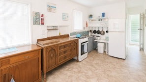 A kitchen with a wooden cabinet, a stove, a refrigerator, and a window with blinds.