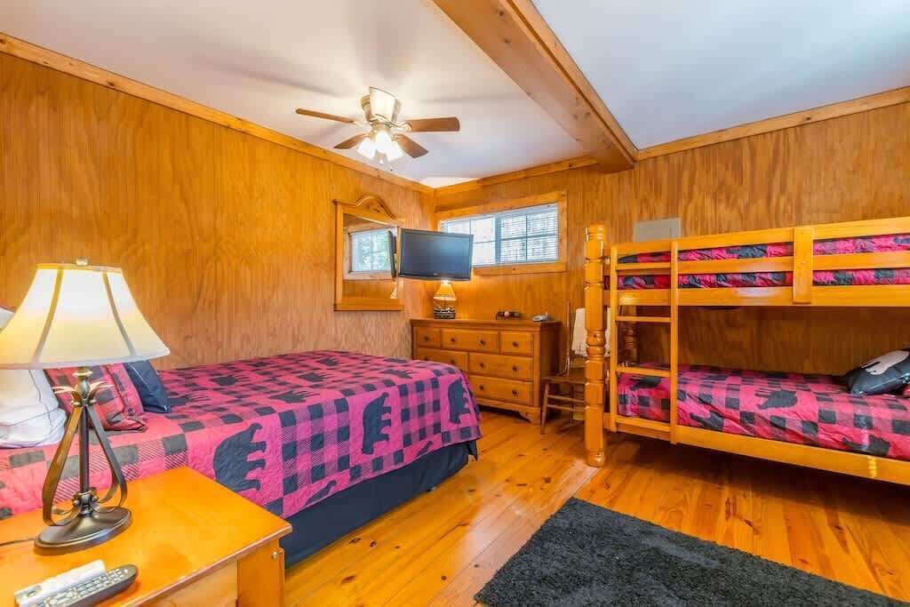 A wooden room with bunk beds, a desk, a television, and a lamp.
