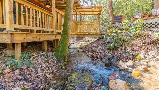 A wooden deck with a wooden railing, a small bridge over a stream, and a forested area.