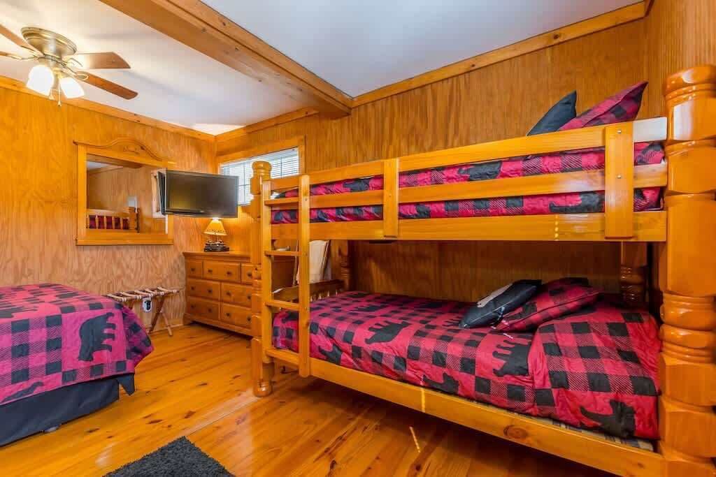 A bunk bed room with wooden walls, a ceiling fan, a TV, and a dresser.