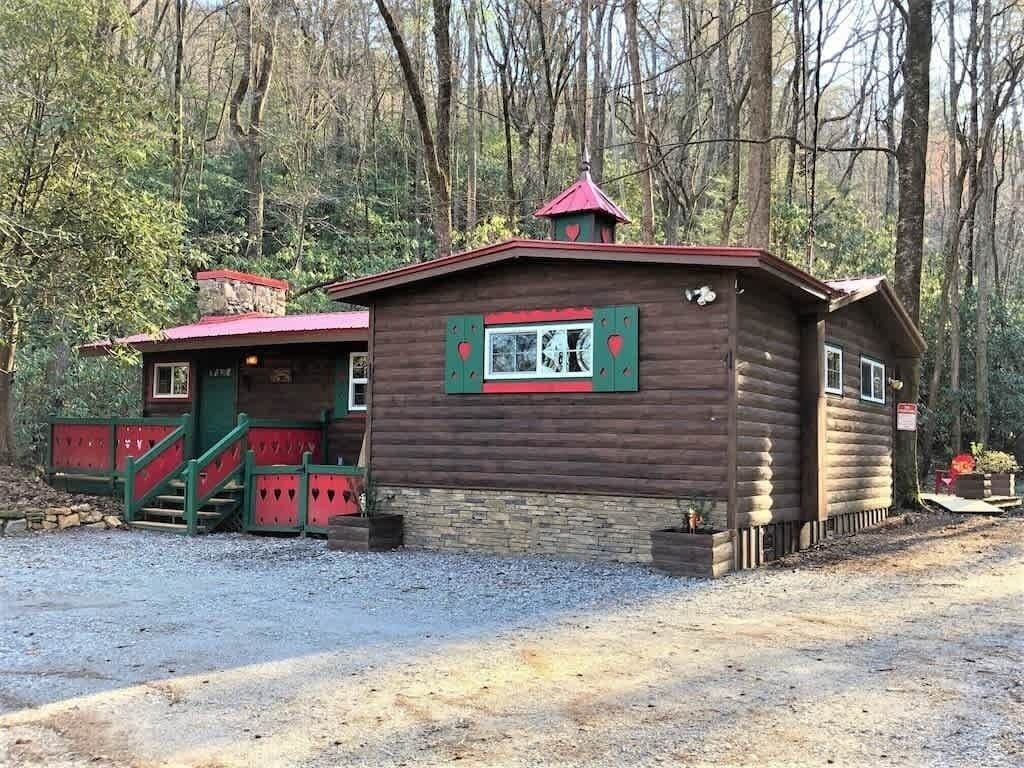 Une cabane en bois avec un toit rouge, un escalier et une fenêtre dotée de volets verts.
