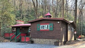 A wooden cabin with a red roof, a staircase, and a window with green shutters.