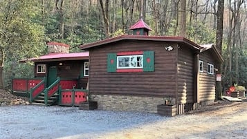 Une cabane en bois avec un toit rouge, un escalier et une fenêtre dotée de volets verts.