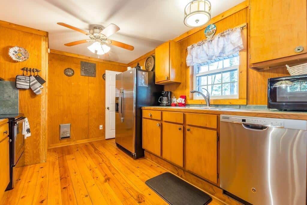 A wooden kitchen with a refrigerator, dishwasher, microwave, and a ceiling fan.