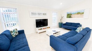A living room with two blue sofas, a white entertainment unit with a flat-screen TV, and a coffee table.