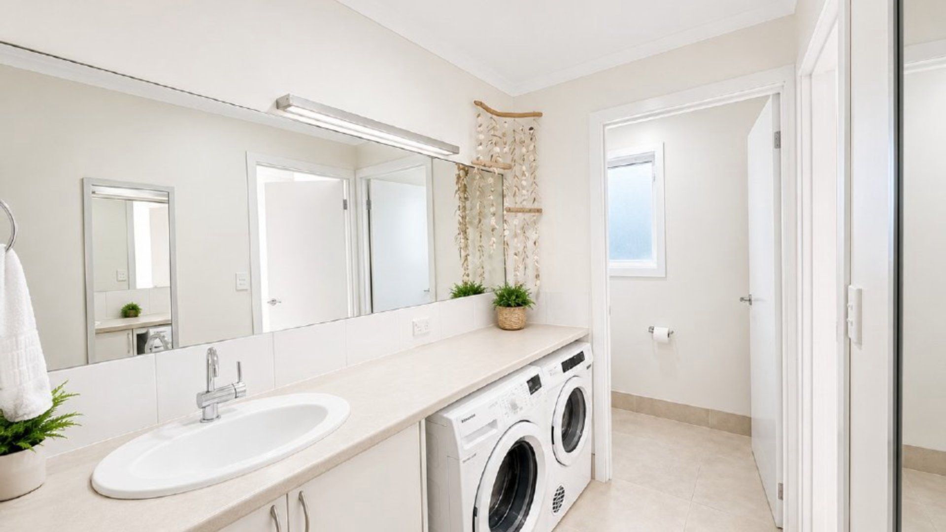 A modern bathroom with a large mirror, a sink, a washing machine, and a potted plant.