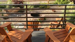 Une terrasse en bois avec deux chaises en bois et une rambarde en métal, donnant sur un paysage rural avec des bâtiments et des arbres.