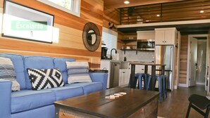 Un salon moderne avec un canapé bleu, un plafond en bois et un coin cuisine équipé d’un réfrigérateur et d’un four à micro-ondes.
