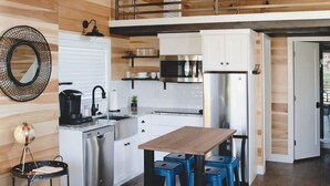 Une cuisine moderne avec des meubles blancs, des appareils en acier inoxydable et une table à manger en bois, accompagnée de tabourets bleus.