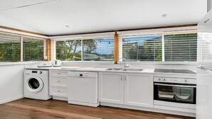 Cozinha moderna com máquina de lavar, lava-louças e forno embutidos, grandes janelas com persianas e vista para o verde lá fora.