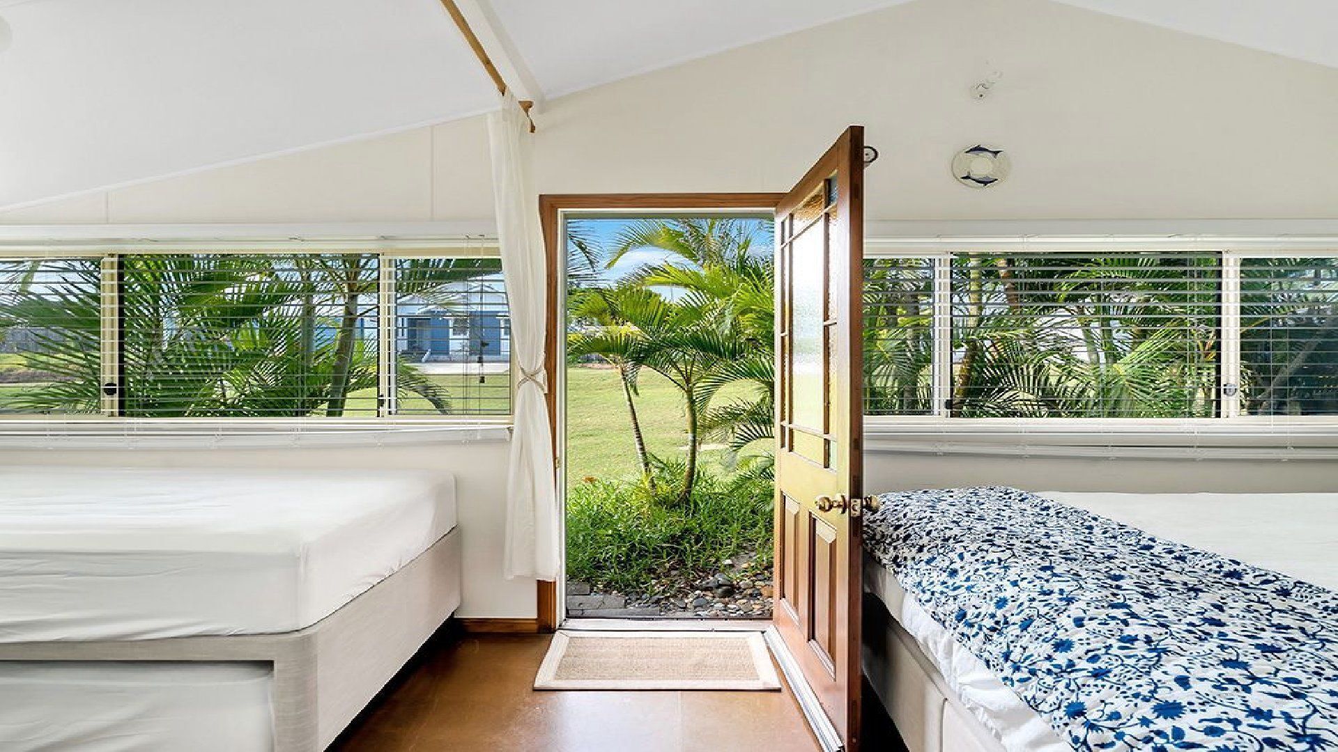 A room with two beds, a door leading to a balcony, and a view of greenery outside.