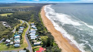 Uma área residencial costeira com casas ao longo da praia, uma estrada serpenteando pela propriedade e vista para o oceano.