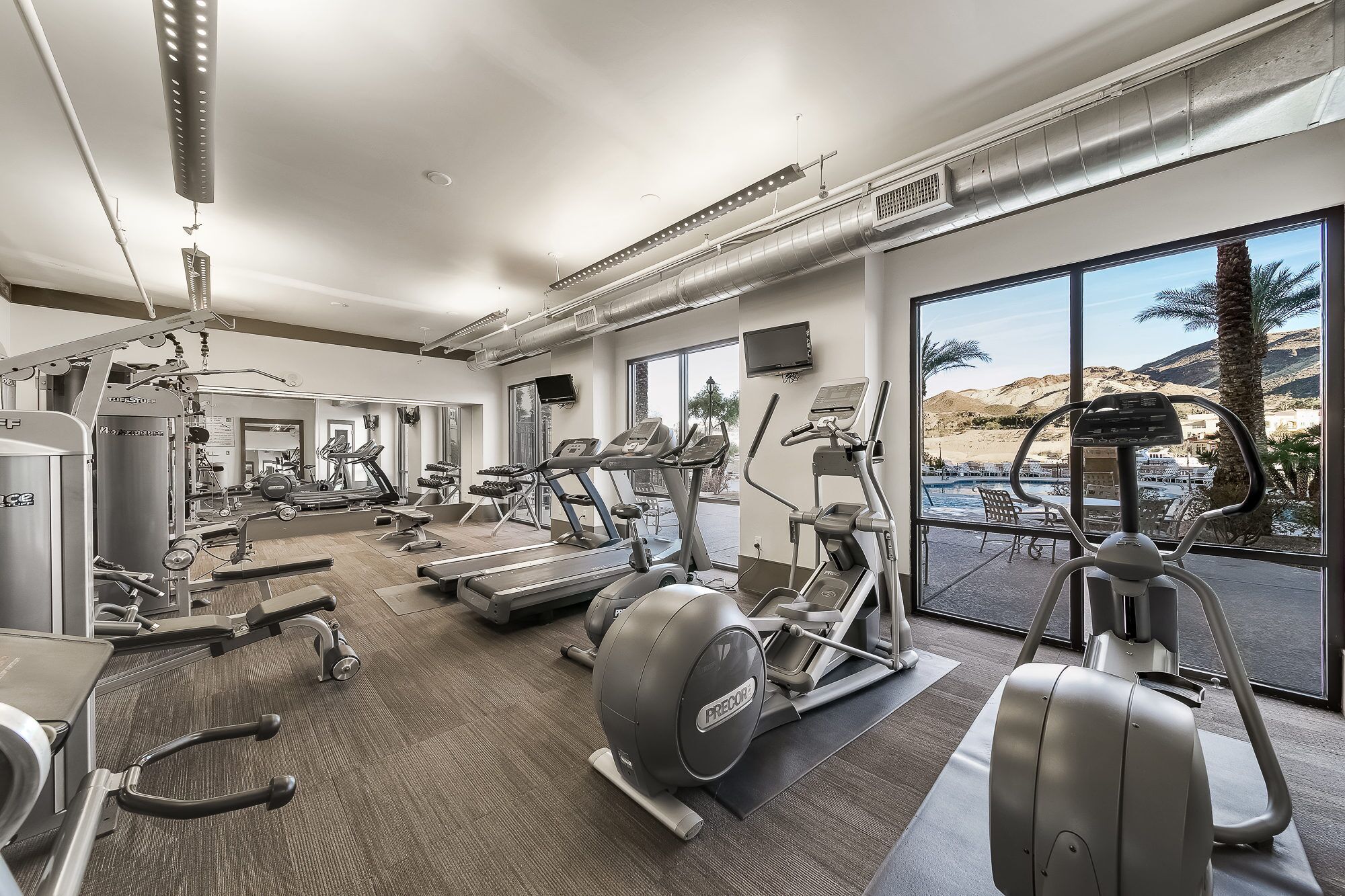 Een moderne sportschool met diverse fitnessapparatuur, grote ramen met uitzicht op een bergachtig landschap.