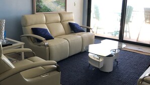 A living room with a beige sofa, a matching armchair, a coffee table, and a painting on the wall. - Oceanfront  Sandcastle Condo, South #506 (Ponce Inlet)