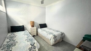 A small, simple room with two single beds, a nightstand, and a lamp. - Seascape Downstairs - Live, relax and play at Seascapes. (Minnie Water)