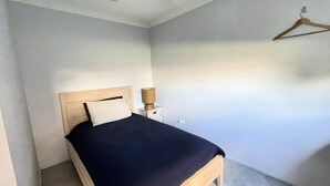 Ein Einzelbett mit Holz Kopfteil und dunkler Bettdecke in einem Zimmer mit hellen Wänden und einem hängenden Holzaufhänger.