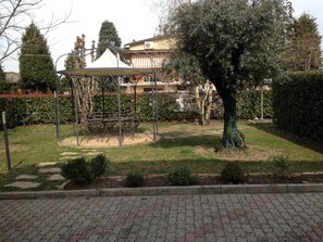 A gazebo with a metal frame and a white canopy, surrounded by a well-maintained lawn and a hedge.