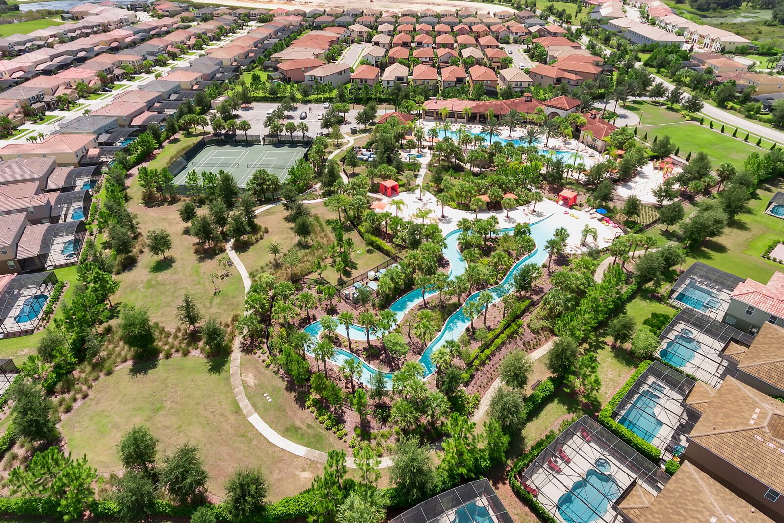 Vue aérienne d’un quartier résidentiel comprenant plusieurs maisons, une piscine centrale avec un toboggan et un court de tennis.