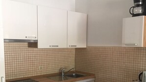Ett kompakt kök med vita skåp, en diskho, en diskmaskin och en kaffemaskin.