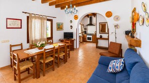 A dining area with a wooden table and chairs, a blue sofa, and a kitchen in the background. - Alcoraia 408 traditional finca with private pool, terrace, barbecue and air conditioning (Campos)