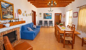 Un salón con un sofá azul, una chimenea, un comedor con muebles de madera y un cuadro en la pared.