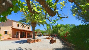 A building with a covered patio, a palm tree, and a gravel courtyard. - Alcoraia 408 traditional finca with private pool, terrace, barbecue and air conditioning (Campos)