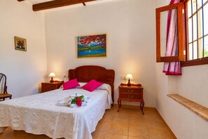 Quarto com cama, duas mesas de cabeceira, um criado-mudo, uma janela com cortinas e um quadro na parede.