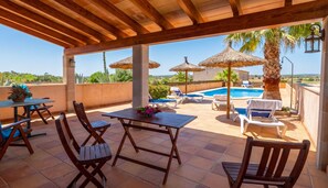 Un espacio al aire libre techado con piscina, sillones de descanso y sombrillas.