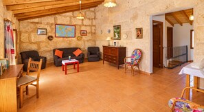 Uma sala de estar aconchegante com teto de madeira, um sofá, uma poltrona, uma mesinha e uma cadeira colorida.