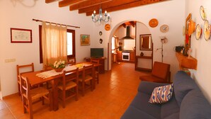 A cozy living room with a wooden dining table, chairs, a blue sofa, and a kitchen in the background. - Alcoraia 408 traditional finca with private pool, terrace, barbecue and air conditioning (Campos)