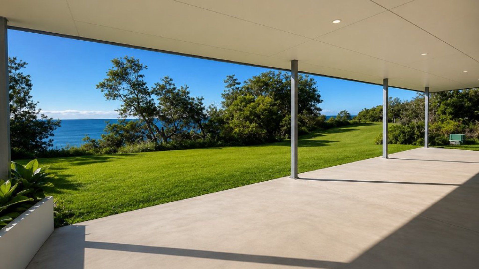 A covered outdoor area with a view of the sea, a grassy lawn, and trees.
