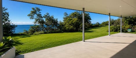 A covered outdoor area with a view of the sea, a grassy lawn, and trees.
