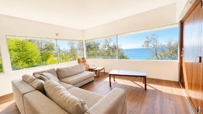 A modern living room with a sectional sofa, a wooden coffee table, and a view of the sea through large windows.