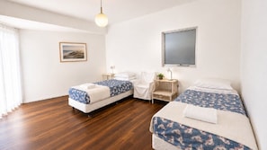 A hotel room with two beds, a window, a picture on the wall, and a wooden floor.