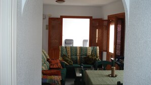 A dining area with a table set for two, a sofa with cushions, and a wooden door with a lattice design. - APTO, WIFI in ACANTILADO 'VIEW TO THE SEA'. PARKING (Aguilas)