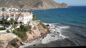 A coastal town with white buildings, a rocky shoreline, and a mountain in the background. - APTO, WIFI in ACANTILADO 'VIEW TO THE SEA'. PARKING (Aguilas)