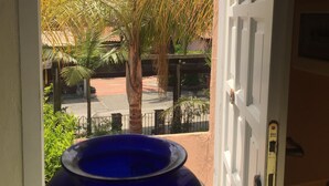 A view through an open door to a courtyard with palm trees and a street.