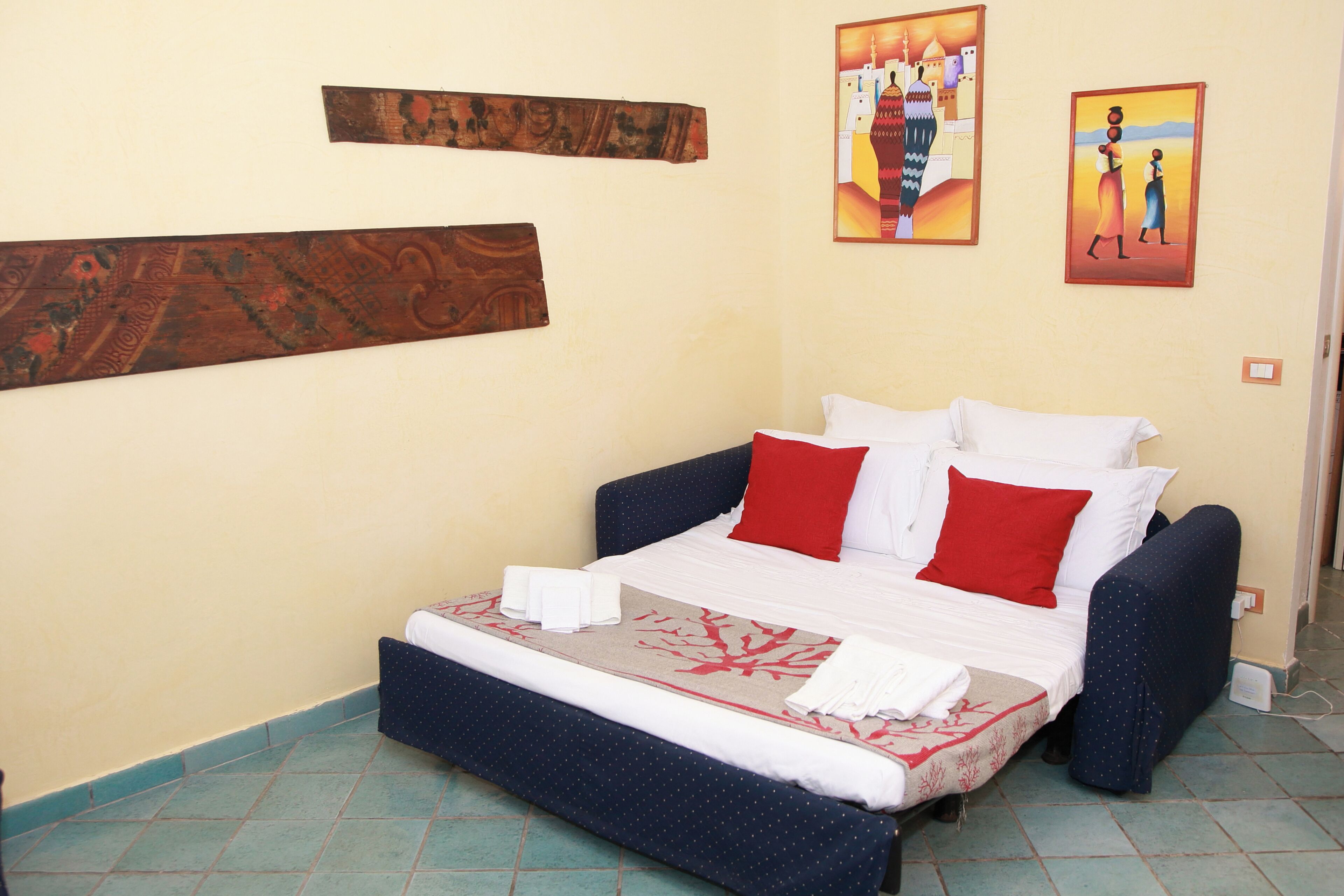 Uma cama com roupa de cama branca e vermelha, cabeceira azul e uma pequena mesa de cabeceira com uma toalha branca.