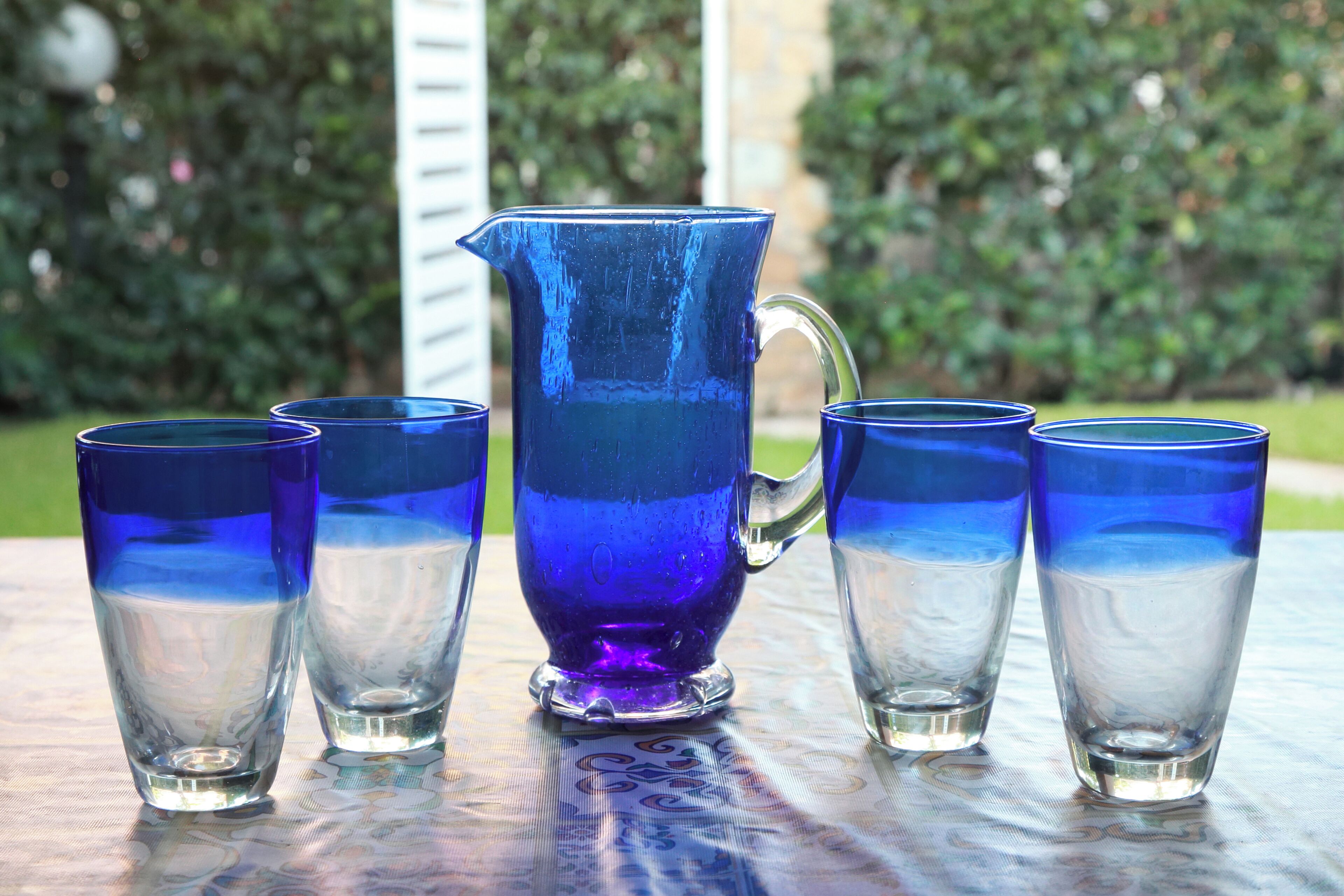 A pitcher and four glasses on a table with a patterned tablecloth.