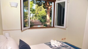 A bedroom with a bed, pillows, a window, and a view of trees and a house.