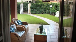 A patio with wicker furniture and a glass-top table, a stone pillar, and a well-maintained lawn.