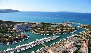 Vista aérea de un puerto deportivo con numerosas embarcaciones amarradas, rodeado de edificios residenciales y un gran hotel.