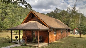Eine Blockhütte mit überdachter Veranda, einem kleinen Anbau und einem Rasen.